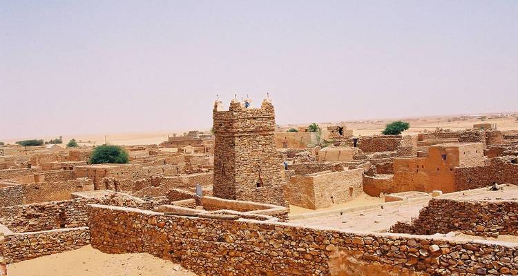Historische Wüstenstadtlandschaft mit zentralem steinernem Minarett am Platz und endlosem sandigem Horizont.