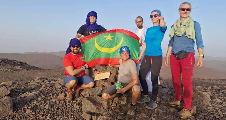 Wandergruppe posiert mit mauritanischer Flagge auf felsigem Gipfel in Wüstengebirgen