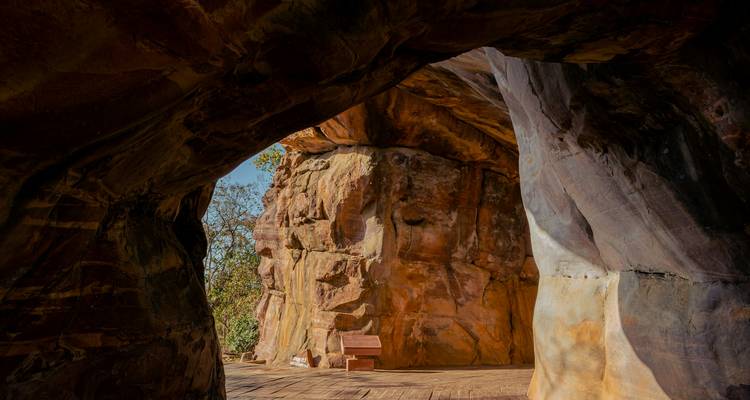 Interior of a weather-worn sandstone cave with striated walls and a wooden bench on the cave floor.
