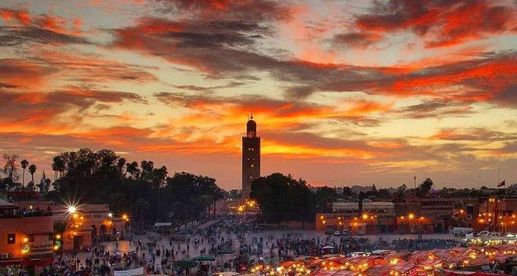 Vibrante atardecer sobre la plaza Jemaa el-Fnaa con la Mezquita Koutoubia silueteada y las luces del mercado brillando.