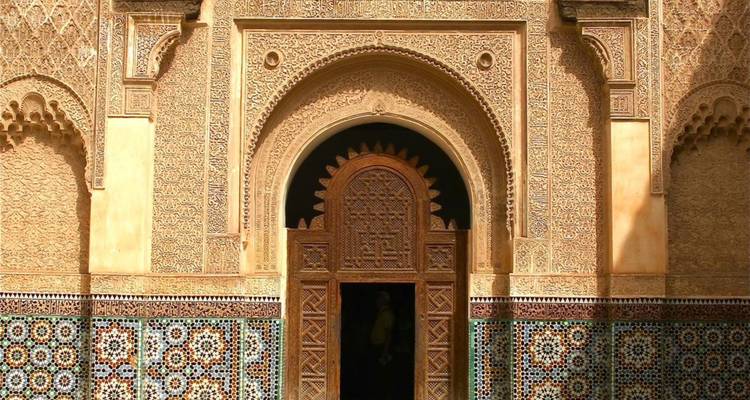 Entrada marroquí ornamentada con estuco intrincado, azulejos de mosaico y una puerta de madera tallada.
