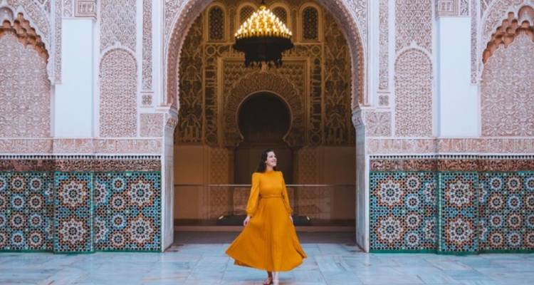 Mujer con un vestido amarillo fluido gira bajo un arco ornamentado y mosaicos coloridos en un patio marroquí.
