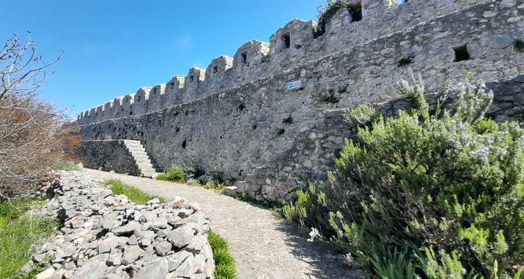 Largo muro de fortaleza de piedra con almenas espaciadas uniformemente serpentando a lo largo de un sendero en la ladera