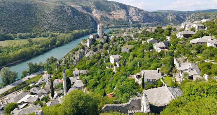 Ladera exuberante salpicada de casas de piedra y una torre medieval que domina un río sinuoso