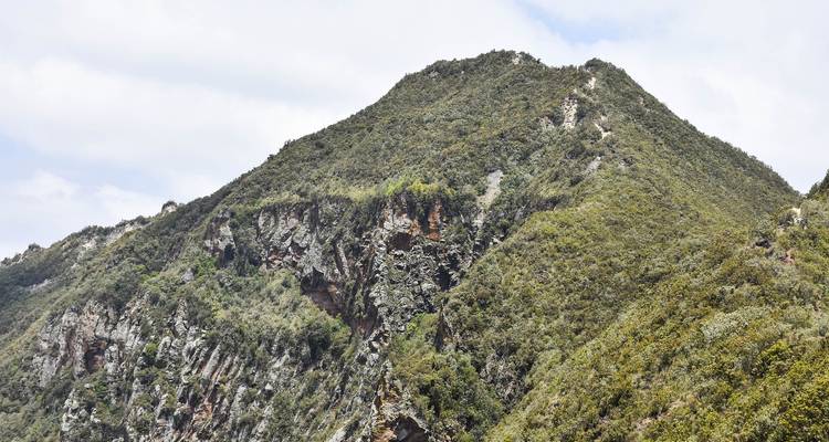 Un pic de montagne vert et escarpé avec des parois rocheuses abruptes sous un ciel partiellement nuageux.