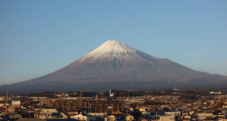 Le mont Fuji se dresse au-dessus d'une ville japonaise, son cône parfait couronné de neige fraîche dans la lumière dorée du matin.