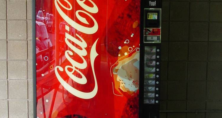 Coca-Cola-Marken-Verkaufsautomat vor gefliester Wand.