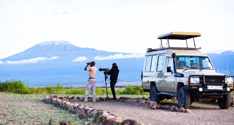 Twee safarireizigers fotograferen Kilimanjaro vanaf naast een terreinvoertuig op de open vlaktes.