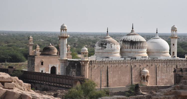Complexe de mosquée historique aux dômes blancs situé au milieu de plaines arides et de murs de fort en ruines.