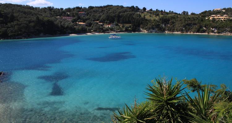 Baie turquoise cristalline bordée de collines luxuriantes avec un seul yacht flottant au centre.