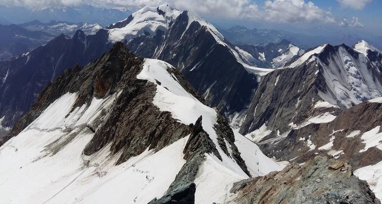 Vue aérienne des lignes de crête alpines spectaculaires recouvertes de neige sous une lumière d'été éclatante.