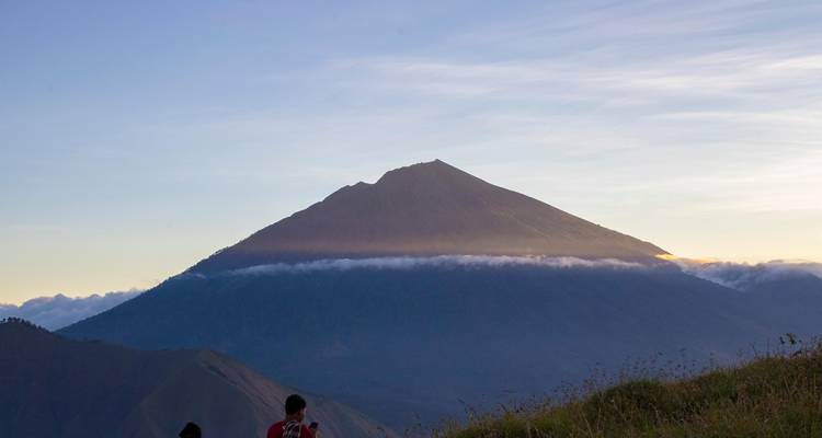 Silhouette de montagne en forme de cône à l'aube avec une bande de nuages épousant sa pente.
