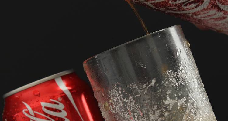 Prise de vue en studio d'un cola versé d'une canette dans un verre givré sur fond noir.