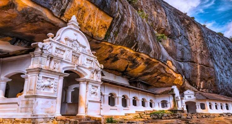 Weiß getünchte Fassade des Dambulla-Höhlentempels, der in eine massive überhängende Felswand hineingebaut wurde.