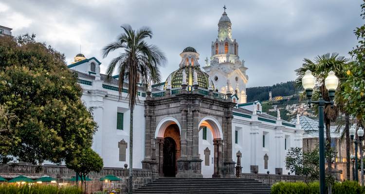 Historic white stone church with ornate green-tiled dome and palm trees in colonial Quito.