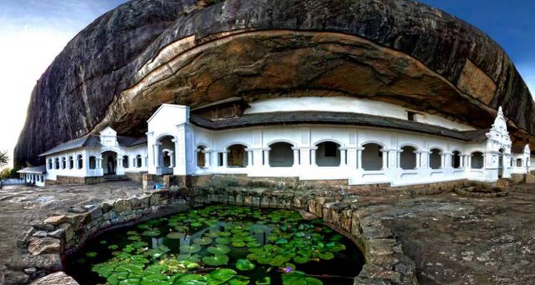 Witboogige Dambulla grottempel genesteld onder een enorme rotsoverhang bij een lelievijver