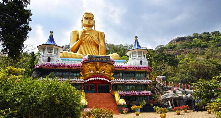 Torenhoge gouden zittende Boeddha boven de kleurrijke gevel van de Gouden Tempel van Dambulla
