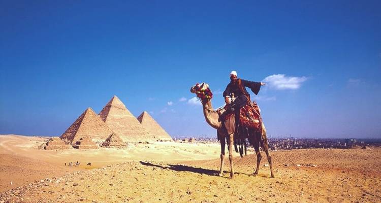 Un jinete de camello contempla las tres pirámides de Giza a través del desierto dorado