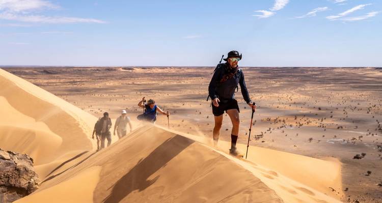 Groupe de randonneurs gravit une crête de dune de sable escarpée avec de vastes plaines sahariennes s'étendant au-delà.