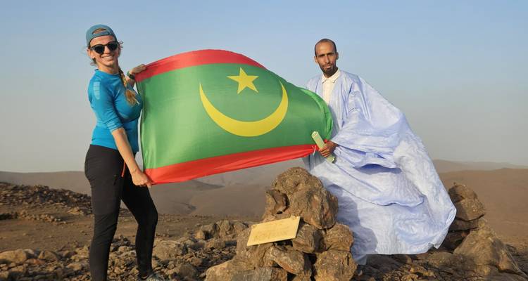 Aventureros sosteniendo la bandera mauritana en la cima rocosa con valles desérticos detrás