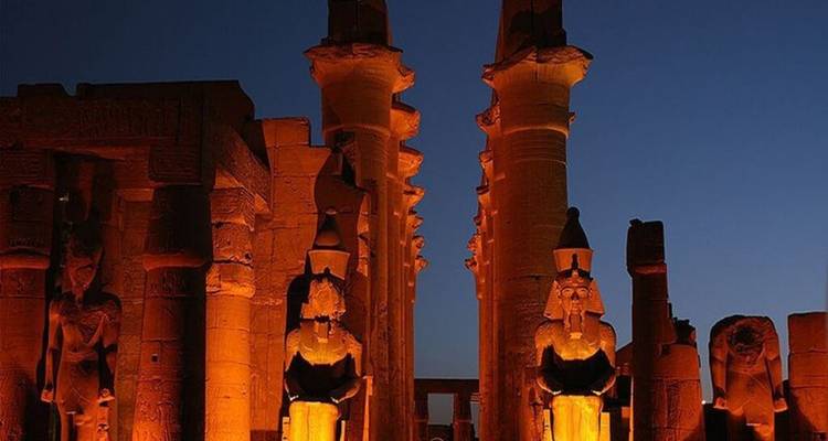 Beleuchtete Säulen und sitzende Pharaostatuen des Luxor-Tempels, die in der Nacht leuchten.