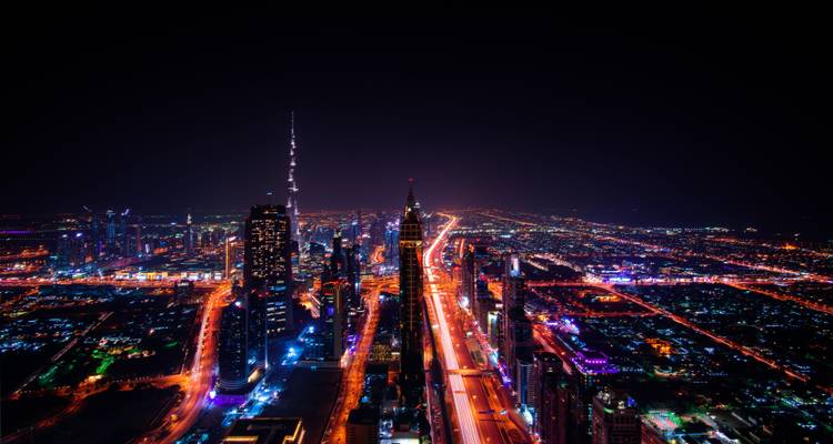 Vue nocturne centrée le long de la route Sheikh Zayed de Dubaï avec des traînées de lumière néon et un horizon lointain.