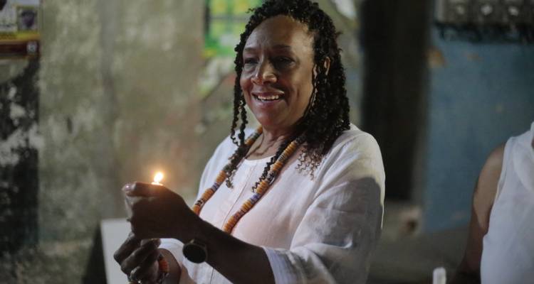 Femme souriante vêtue de blanc tenant une chandelle allumée lors d'une cérémonie en intérieur
