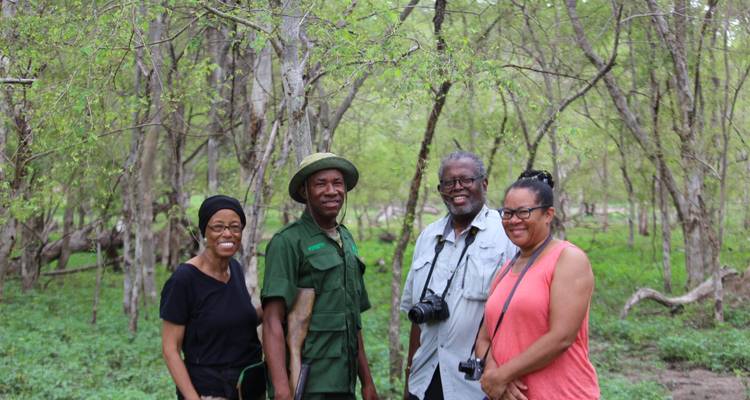 Small group including a uniformed ranger pose in a leafy woodland setting.