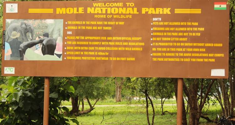 Large wooden welcome sign for Mole National Park set in a green roadside setting.