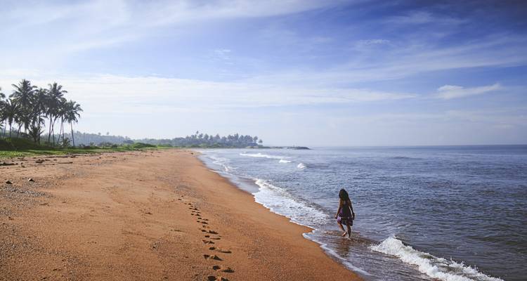 Un voyageur solitaire marche le long d'une plage tropicale déserte laissant des empreintes dans le sable.