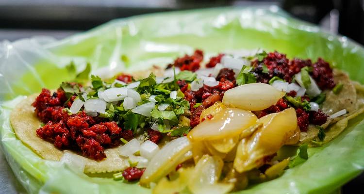 Close-up van taco's belegd met gesnipperde uien, koriander, gemarineerd vlees en gegrilde uien op een groen bord.