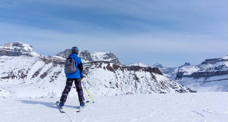 A skier standing on a snowy ridge admiring rugged alpine peaks