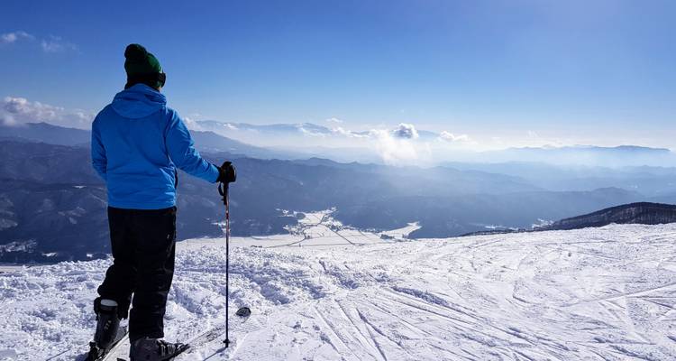 A skier standing on a summit looking out over layers of snowy mountain ranges