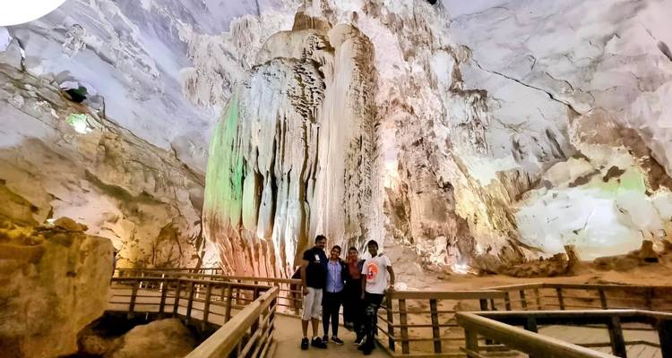 Vier bezoekers poseren in een verlichte kalksteengroet met hoge stalagmieten en stalactieten.