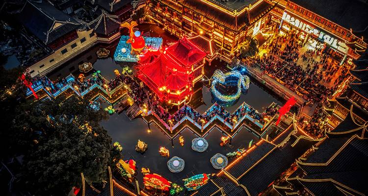 Luftaufnahme des hell erleuchteten Laternenfesters im Yuyuan-Garten mit einer kunstvollen Zickzack-Brücke.