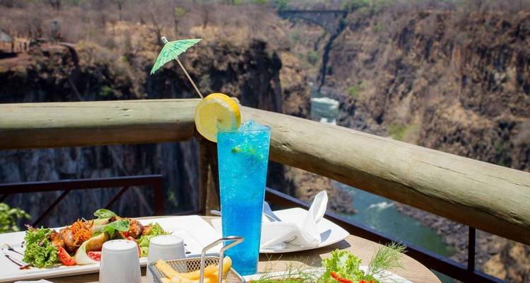 Un cocktail bleu vif et des mets sur un balcon surplombant un profond canyon fluvial
