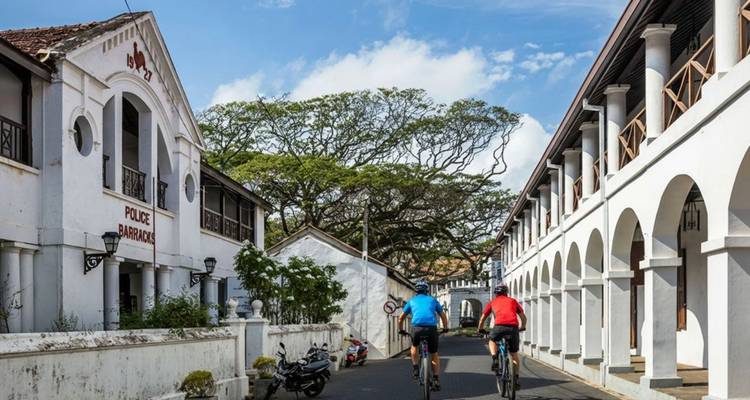 Two cyclists riding through a narrow colonial street lined with whitewashed buildings inside Galle Fort, Sri Lanka.