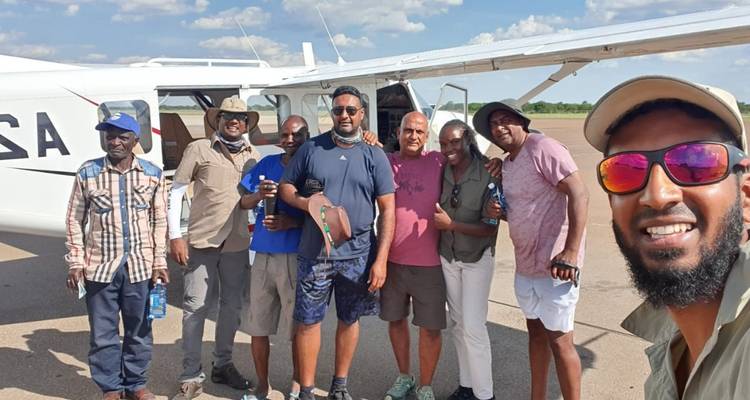 Travel group posing happily beside a small charter plane on an airstrip under blue skies.