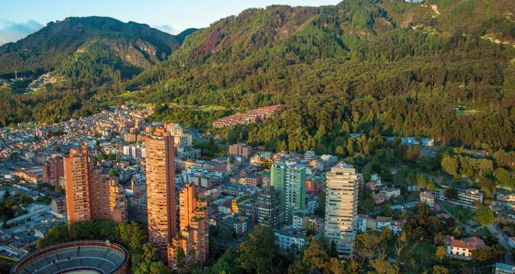 Luchtfoto van Bogota met hoge appartementstorens op de achtergrond omgeven door weelderige bosrijke bergen.