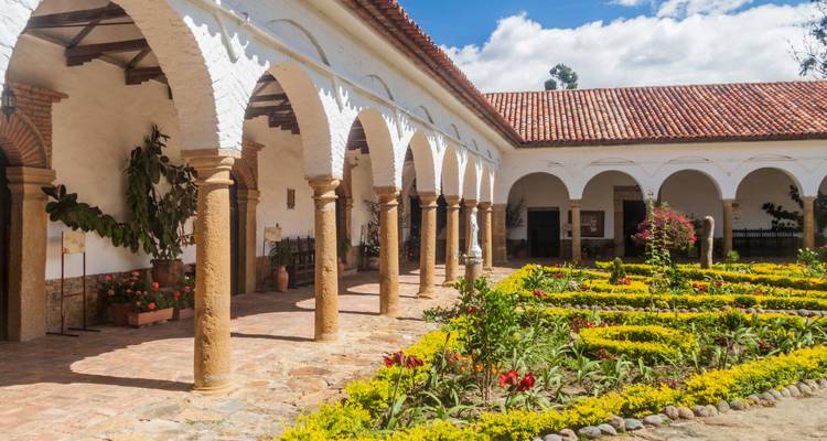 Koloniaal kloosterplein met stenen bogen en kleurrijke bloembedden in Villa de Leyva.