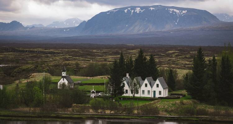 Église blanche isolée et ferme entourées de plaines mousseuses avec des montagnes en arrière-plan