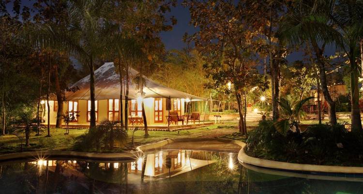 Luxury canvas tent lit up at night beside a reflective swimming pool in the jungle