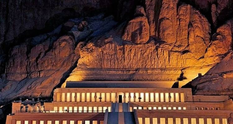 Tempel van Hatshepsut warm verlicht onder de torenhoge rotswand in de nacht.