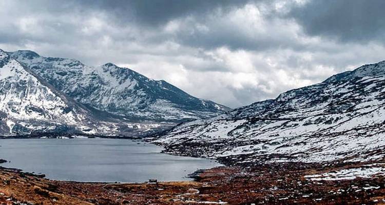 Snow-rimmed alpine lake under dramatic cloudy skies.