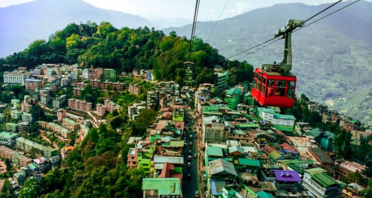 Red cable car glides above a sprawling hillside city with surrounding mountains.