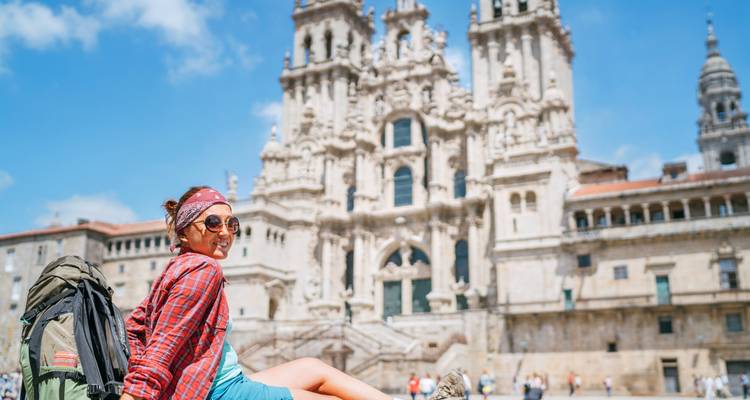 Mochilero sonriente relajándose frente a la famosa catedral de Santiago en un día soleado