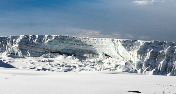 Aufragende, blauweiße Gletscherwand und schneebedeckter Untergrund unter einem klaren Himmel in der Nähe des Gipfels des Kilimandscharo