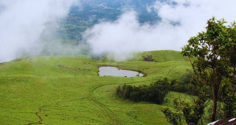 Les Highlands brumeux et verdoyants avec un petit étang en forme de cœur aperçu au-dessus des nuages.