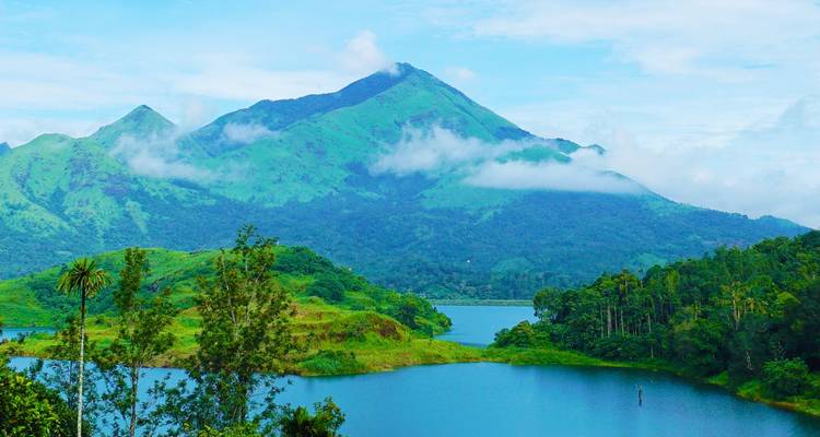 Une montagne verdoyante se reflétant dans un réservoir bleu avec des volutes de nuages enveloppant les pentes.