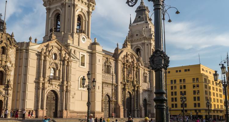 Nahaufnahme der Fassade der Kathedrale von Lima, die im Licht des späten Nachmittags erleuchtet ist, mit Besuchern im Vordergrund.